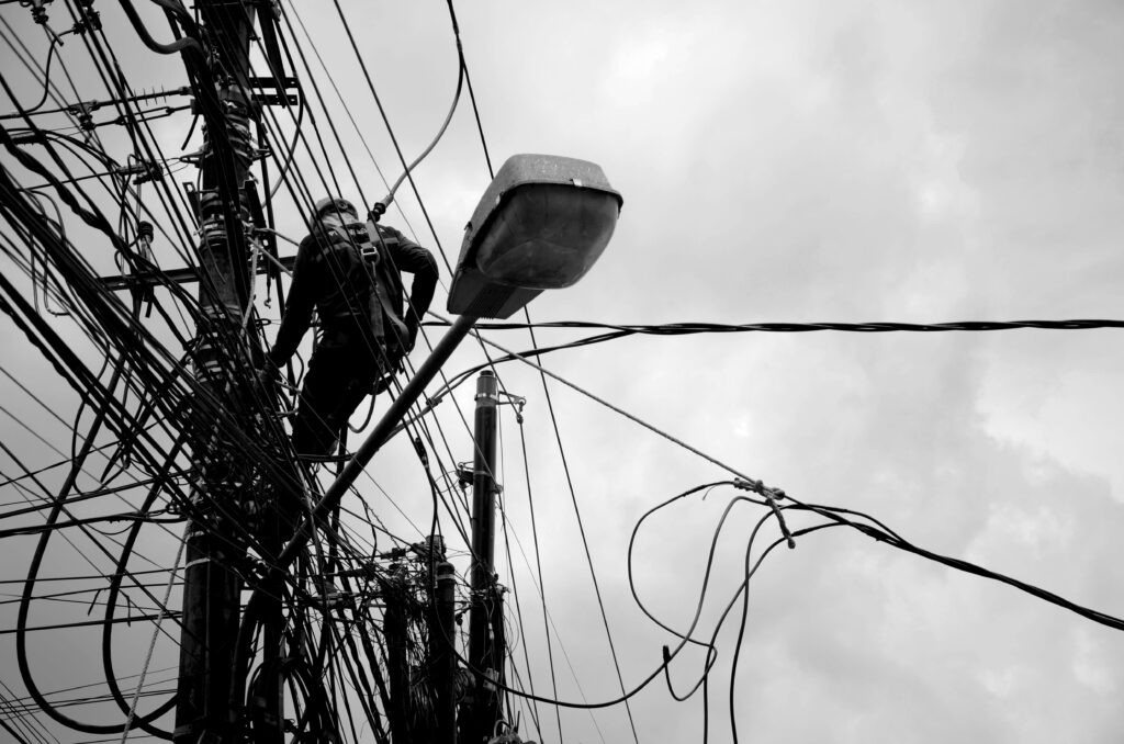 Black and white image of a technician working on power lines, illustrating electrical repair work.