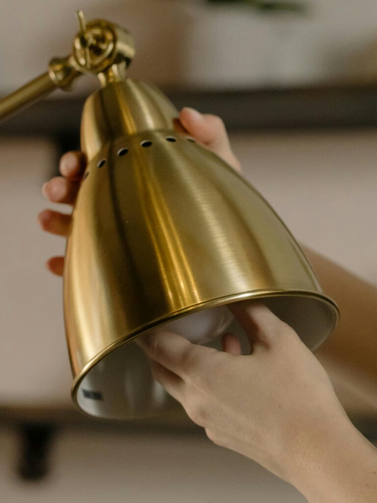 Close-up of hands fixing a light bulb into a modern brass desk lamp, showcasing home maintenance.